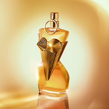 Jean Paul Gaultier Gaultier Divine Parfumflakon in goldener Korsettform vor leuchtend warmem Hintergrund, elegant auf spiegelndem Untergrund inszeniert.