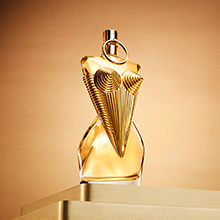 Jean Paul Gaultier Parfumflakon in goldener Korsettform, kunstvoll designt und elegant auf goldfarbenen Stufen vor warmem Hintergrund präsentiert.
