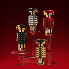 Mehrere Fame Parfumflakons von Rabanne im Roboterdesign mit goldenen und roten Elementen auf transparenten Podesten vor rotem Hintergrund.